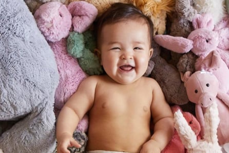 A laughing baby laying on a pile of stuffed animals